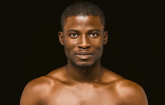 Nude smiling African macho man posing on black background, portrait of an attractive African american man smiling slightly while looking at the camera. Toned image