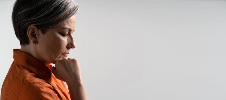 Sad or depressed mature woman thoughtfully touches her chin with hand. Profile view. Cut out on white background. Copy spase for text. Horizontal template for ad banner