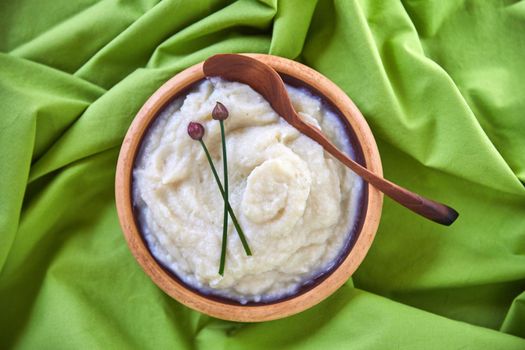 Our food should be our medicine and our medicine should be our food. Overhead shot of cauliflower mash puree in a wooden bowl on a green tablecloth.