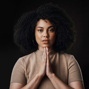 I believe. Cropped portrait of an attractive young woman in prayer against a dark background in studio.