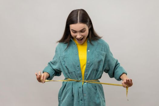 Woman holding tape line on her waist, being amazed with her body parameters after slimming.