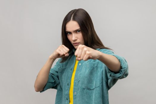 Woman standing with clenched fists and furious look, ready to punch, expressing aggression.