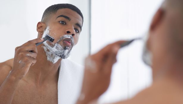 A fresh shave is all I need. a handsome young man standing and using his bathroom mirror to shave in the morning.