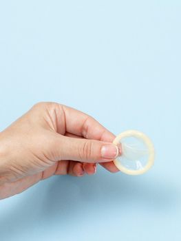 Female hand holding condom on blue background