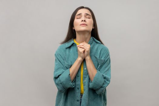 Portrait of pleading young adult woman looking up with hands in prayer sincere saying please apology