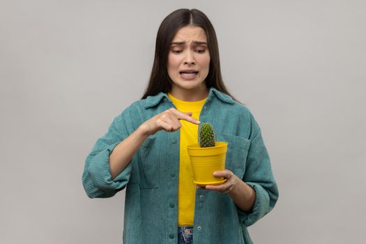 Woman holding potted cactus, trying to touch prickly flower with eyes full of fear and frowning face