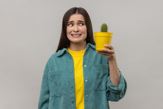 Woman holding prickly cactus, looking at plant with frowning face from ignorance.