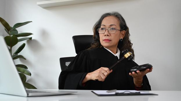 Mature judge or attorney with gavel hammer mallet and consulting online via video conferencing on laptop computer