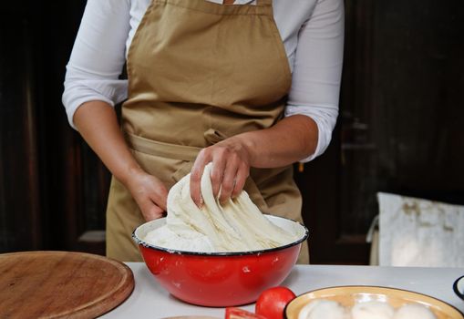 Details: chef's hands kneading raising yeast dough in a vintage enamel red bowl while preparing bread in rustic kitchen