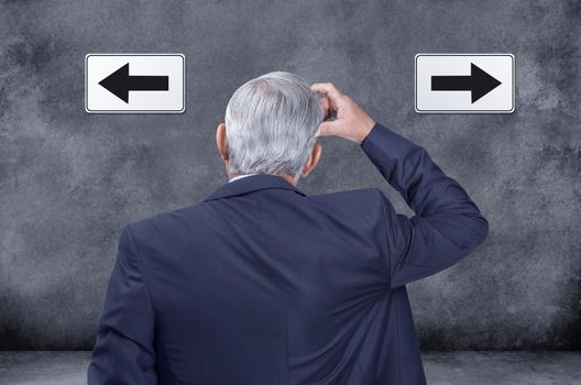 A rear view of thinking, confused and deciding businessman struggling and trying to decide which way to go. Indecisive corporate worker chooses direction with left and right arrow sign on black wall