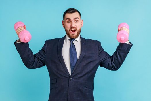 Strong confident businessman wearing official style suit training biceps and triceps with pink dumbbells, screaming, showing his power.