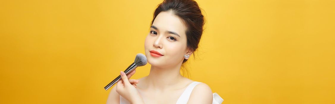 beautiful woman holding makeup brush over yellow