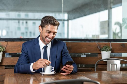 Cheerful male executive browsing cellphone in cafeteria