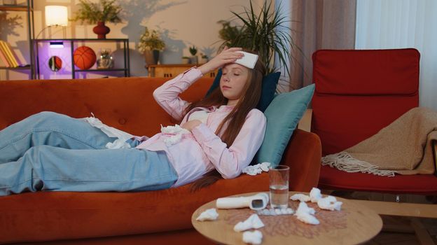 Sick ill child kid suffering from cold or allergy lying on home sofa sneezes wipes snot into napkin