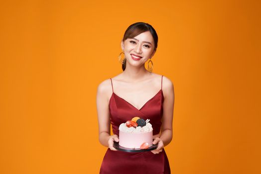 Vertical shot of an elegant woman in a red dress carrying a birthday cake