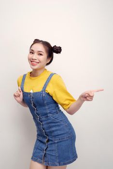 Portrait of asian young girl with two buns pointing fingers aside at copyspace isolated white background