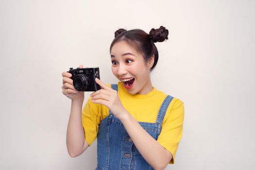 Surprised woman, with top knot hairdo, wearing on denim jumpsuit, holding retro camera, on the white background