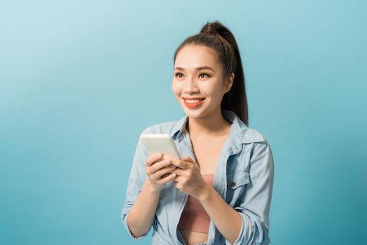 Portrait of a cheerful casual girl holding mobile phone  over blue background