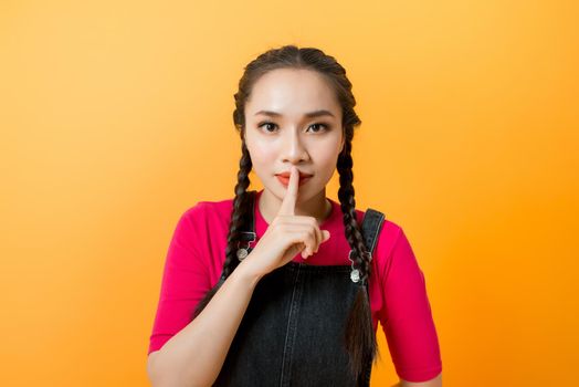 Young Asian girl over yellow background showing a sign of silence gesture putting finger in mouth