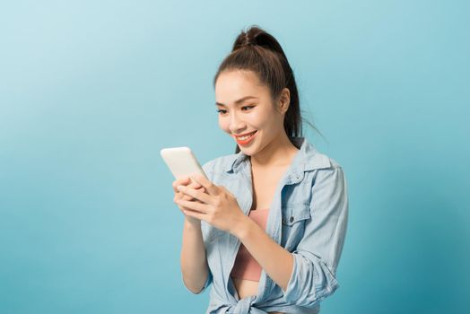 Asian woman 20s holding mobile phone and smiling over blue background