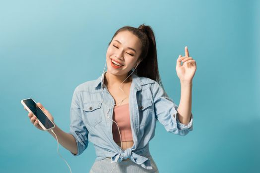 Cheerful woman in headphones listening to music and dancing isolated over blue background