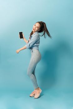 Cheerful young girl listening to music with headphones while jumping and singing over blue background