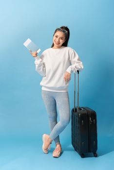 Full length image of Cheerful woman wearing in casual clothing preparing to trip with baggage and tickets over blue background