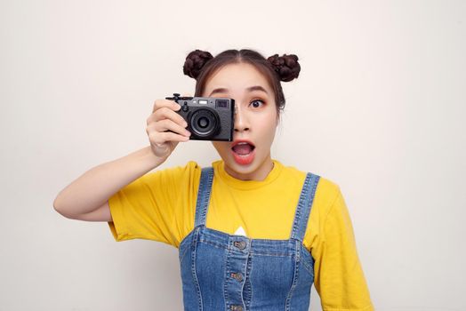 Image of excited paparazzi girl  holding retro camera at face and photographing isolated over white background