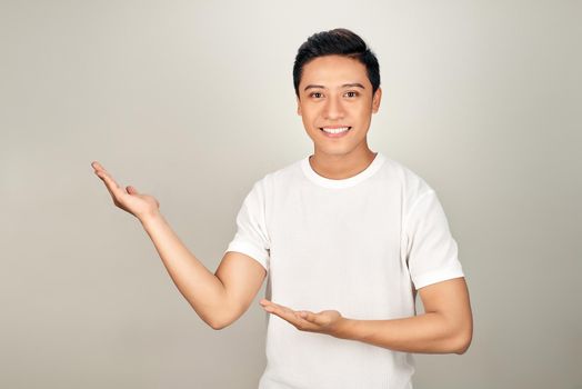 Young handsome man pointing to the side with hand and open palm, presenting ad smiling happy and confident