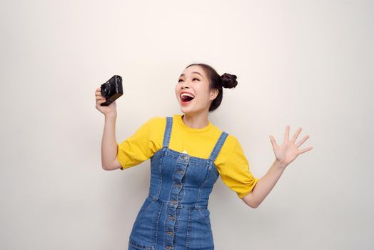 Surprised woman, with top knot hairdo, wearing on denim jumpsuit, holding retro camera, on the white background