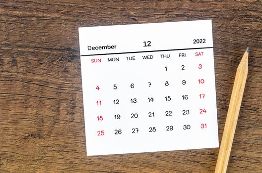 The December 2022 calendar and wooden pencil on vintage wooden background.