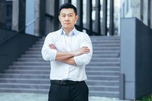 Portrait of serious asian businessman, man outside office looking at camera