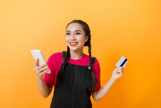 happy asian woman holding credit card and smartphone on colourful background.