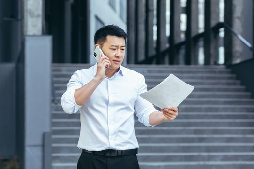 Frustrated insurance agent with documents talking on the phone outside the office