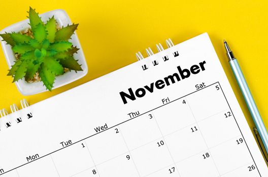 The November 2022 desk calendar and pen with plant pot on yellow background.