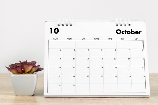 The October 2022 desk calendar with plant on wooden table.