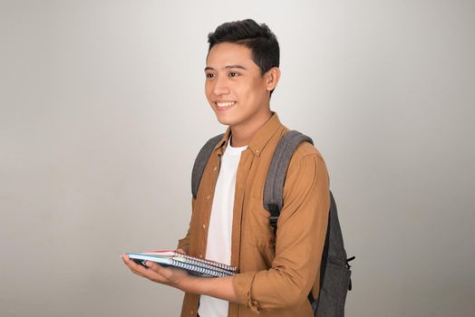 Confident handsome Asian student holding books and smiling at camera