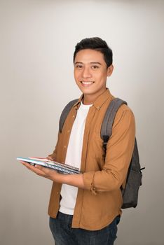 Confident handsome Asian student holding books and smiling at camera