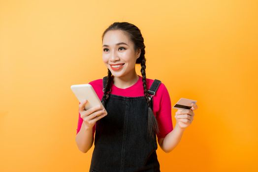 Asian woman use smartphone to payment online shopping with blank credit card, yellow background