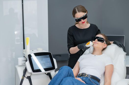 Young caucasian woman in goggles on photorejuvenation procedure. Doctor cosmetologist with a female patient.