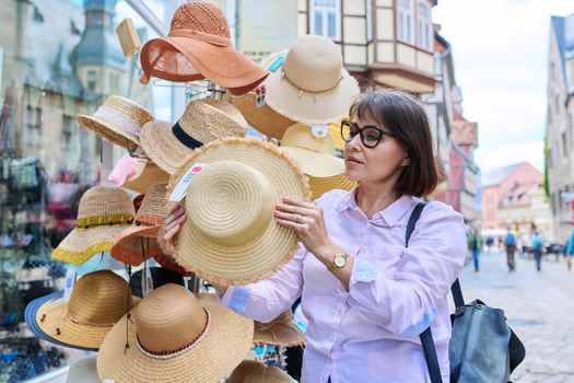 Woman tourist choosing to buy straw hat in store