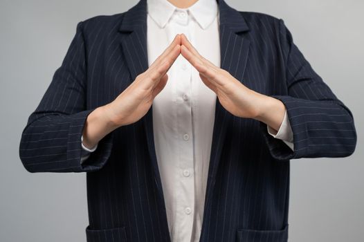 Business woman in a suit holding her hands in the shape of a house.