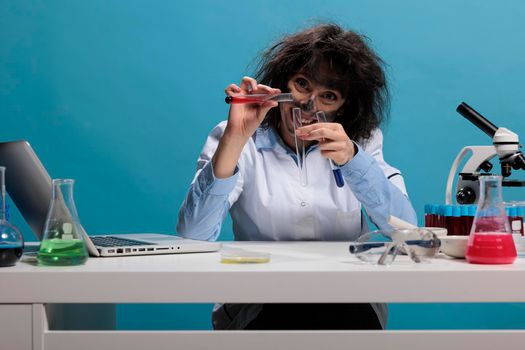 Portrait of crazy chemist with wild look mixing dangerous chemical compounds while sitting at desk