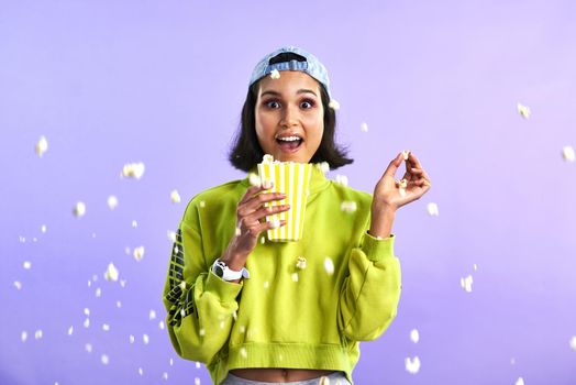 Kernel popping, heart stopping, action packed movies. Studio shot of a beautiful young woman eating popcorn against a purple background.