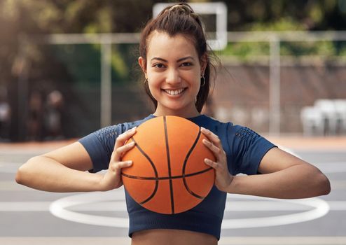 Playing basketball can boost your confidence. Portrait of a sporty young woman holding a basketball on a sports court.