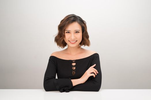Portrait of a cheerful Asian businesswoman sitting at the table on white background