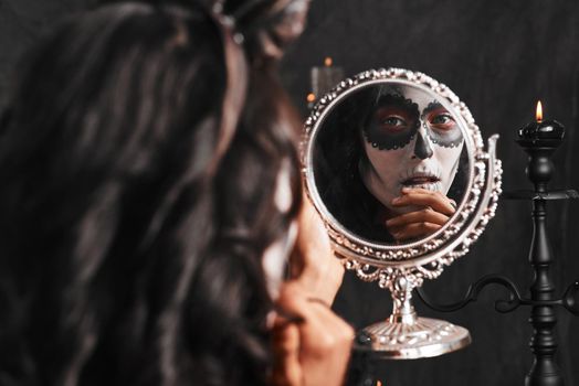 Halloween has arrived. an attractive young woman dressed in her Mexican-style halloween costume looking in a mirror.