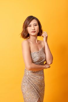 Beautiful female posing in long golden party dress over yellow background