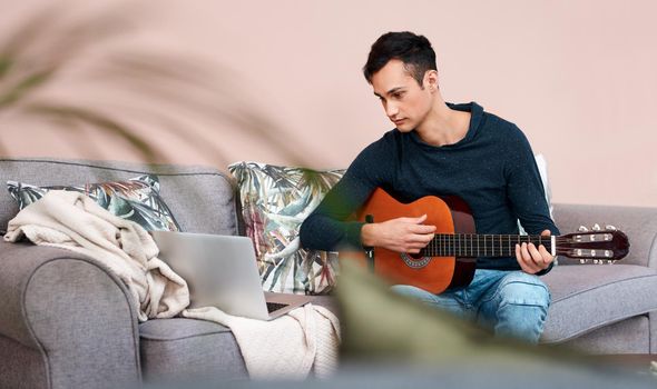 Lockdown done right. a young man using a laptop while playing the guitar at home.