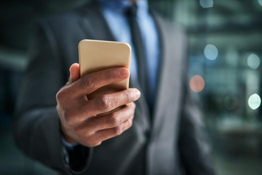 A phone in hand for texting, communication and networking for business planning, discussion and strategy. Closeup of a corporate professional holding a cellphone while standing on a dark background.